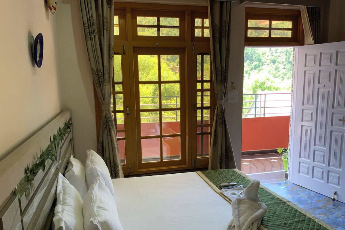 Habitación de hotel con cama, ventana con cortinas y vistas al exterior, además de una puerta con un diseño geométrico.