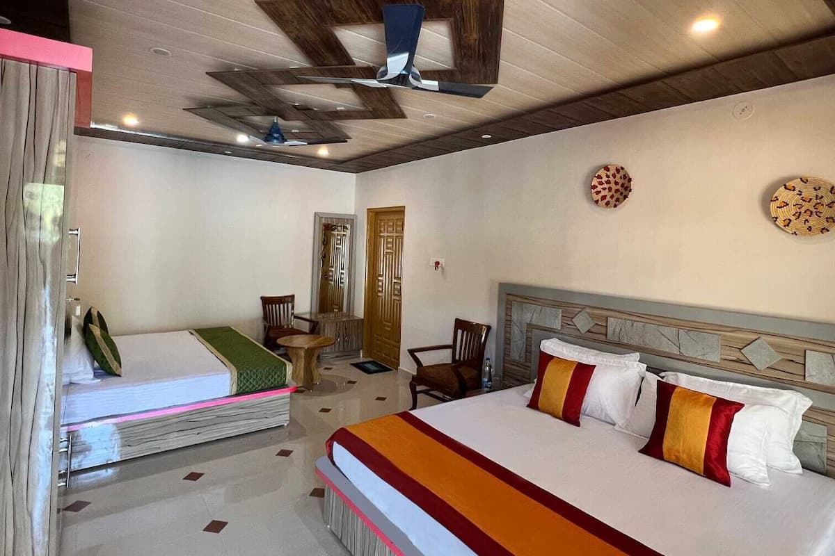 Habitación de hotel con una cama grande, una cama más pequeña, un escritorio y una silla. Hay un ventilador de techo y una puerta en la habitación.