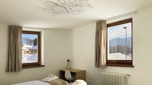 Habitación de hotel con dos camas, un escritorio, una silla, una lámpara y vistas a un paisaje nevado.