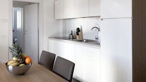A modern kitchen with white cabinets, a stainless steel sink, and a bowl of fruit on the table. - 002 - 4 PAX – TERRACE (LAVARONE)