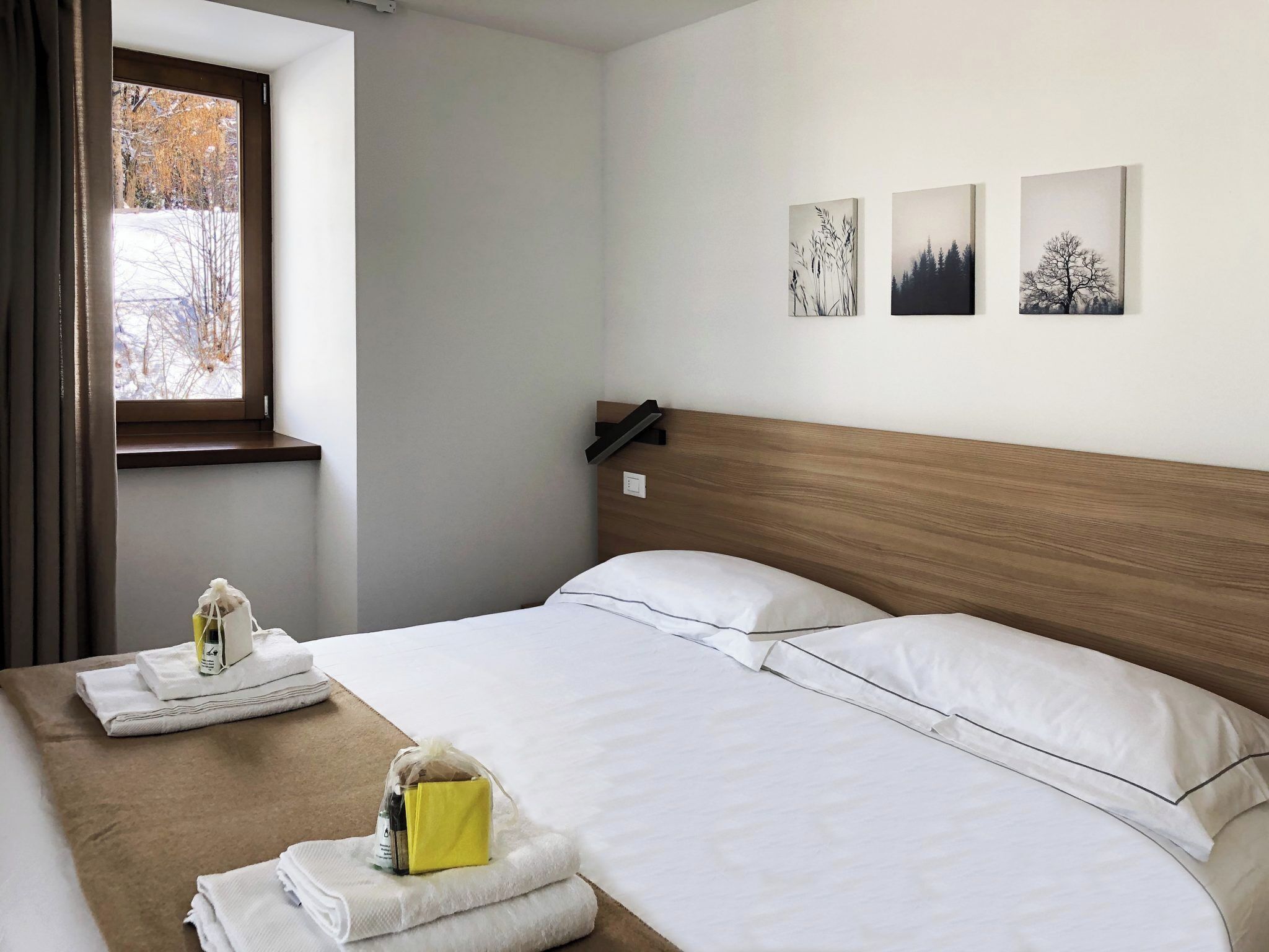 A hotel room with two beds, a window with a view of trees, and three wall-mounted pictures.