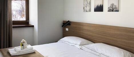 A hotel room with two beds, a window with a view of trees, and three wall-mounted pictures.