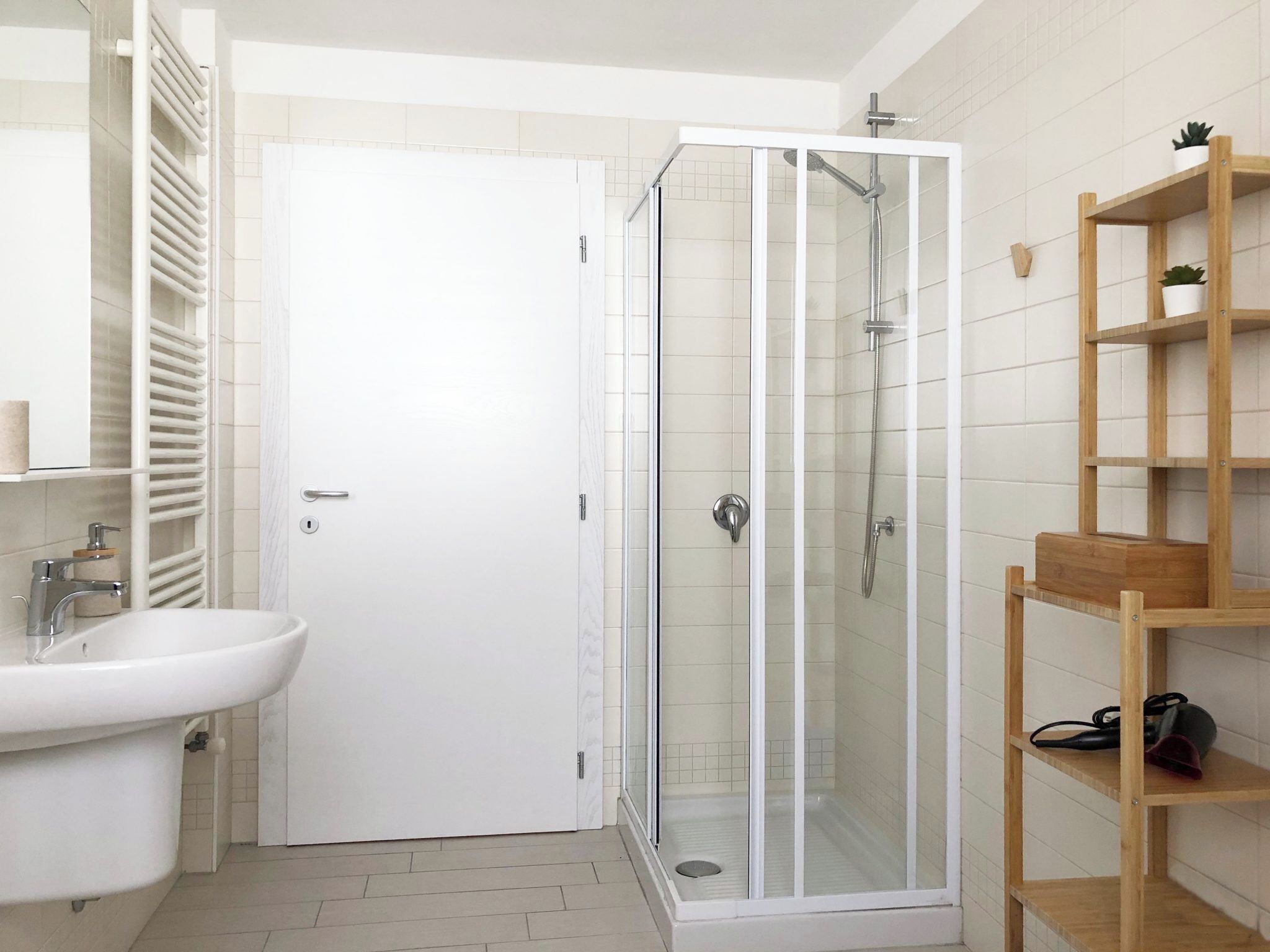 A bathroom with a white sink, a glass-enclosed shower, and a wooden shelf unit.