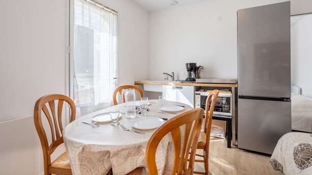 A dining area with a table set for four, a kitchen with a refrigerator, and a window with blinds.