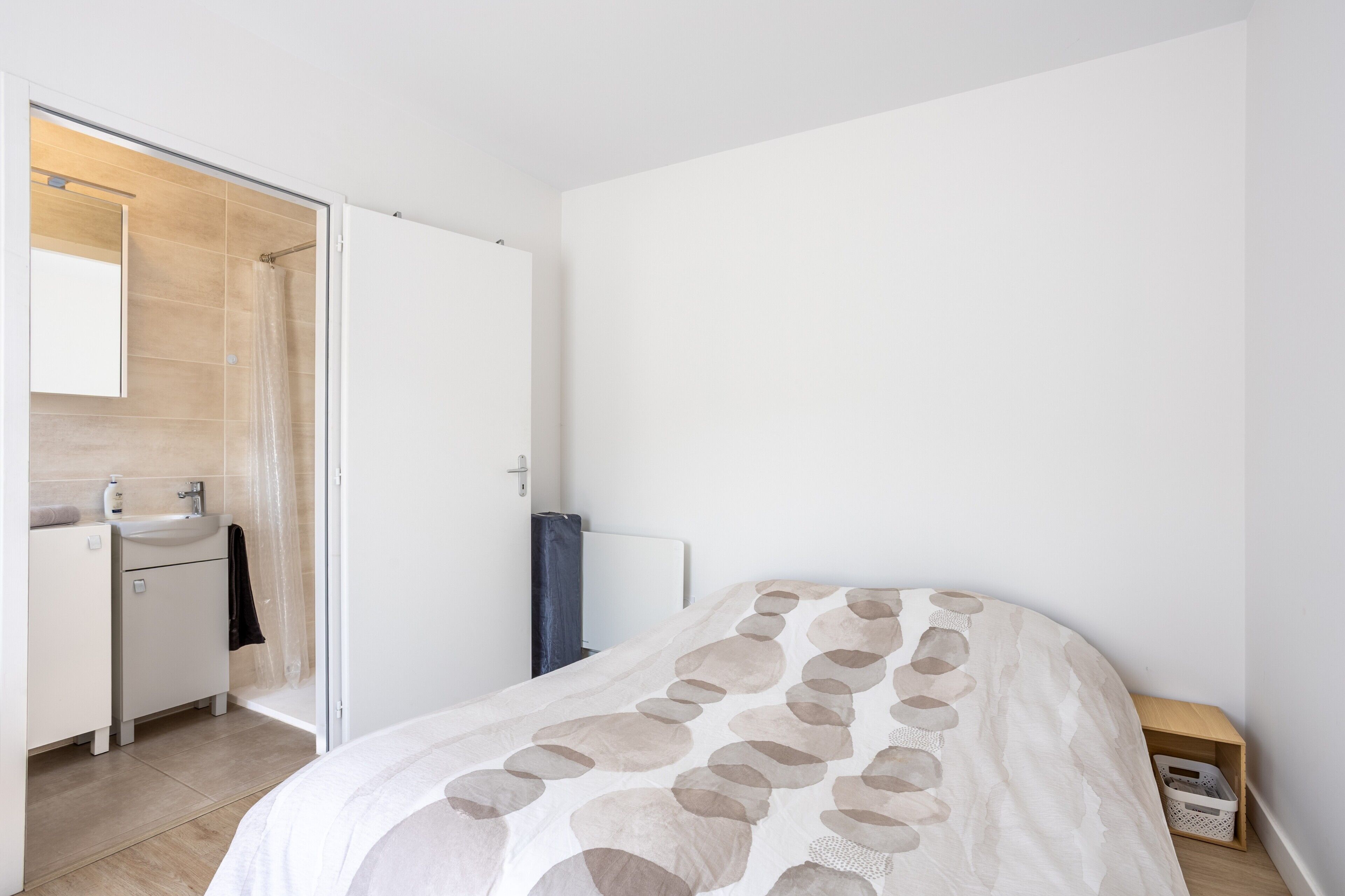 Un dormitorio con una cama, un baño con ducha y una mesita de noche de madera.