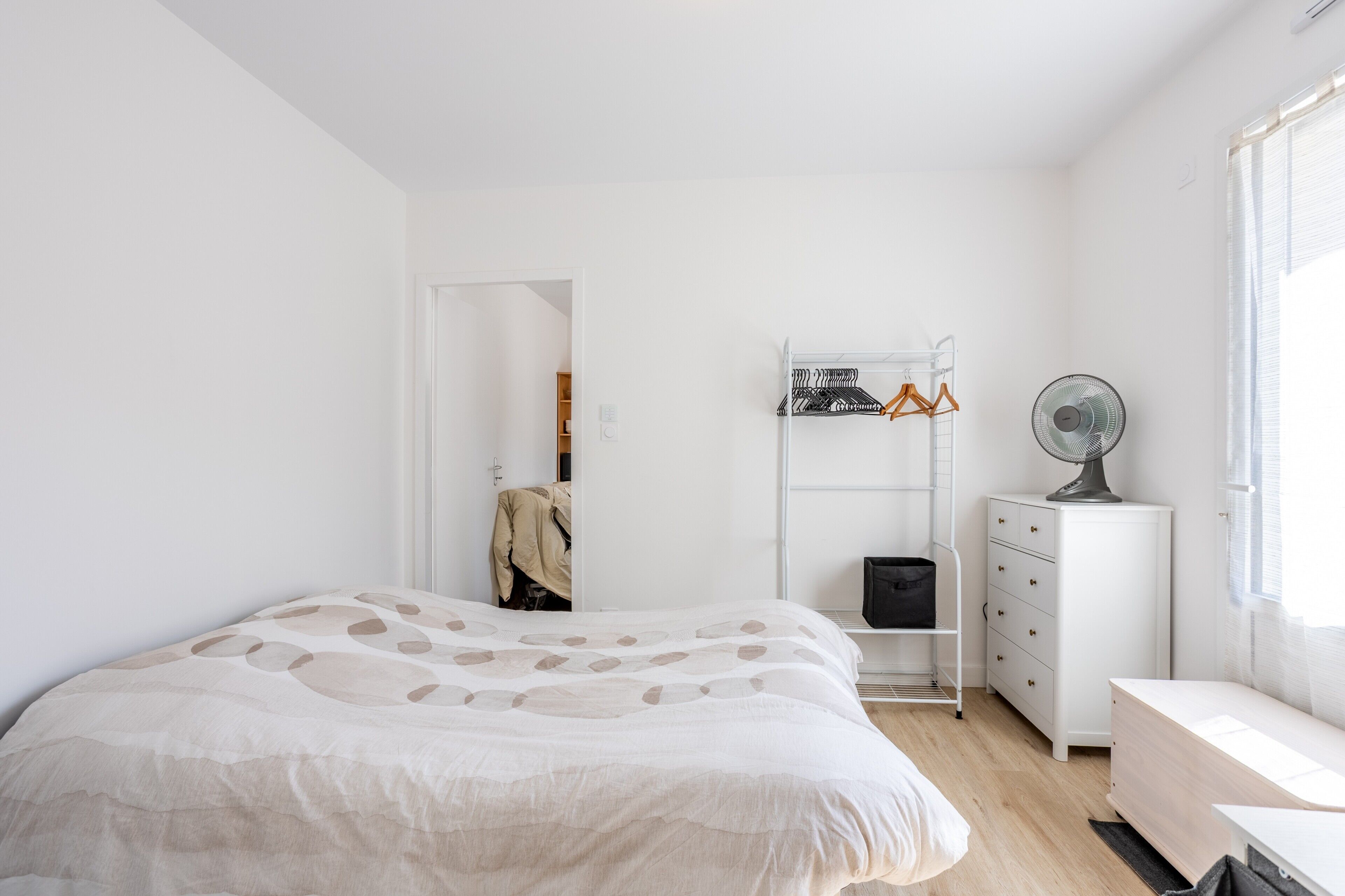 Een slaapkamer met een bed, een kledingkast, een ventilator en een raam.