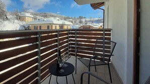 Un balcon avec une balustrade en bois, deux chaises, une petite table et une bouteille de vin.