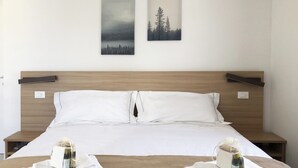 Una cama bien hecha con sábanas blancas, dos almohadas y dos mesitas de noche con botellas y toallas.