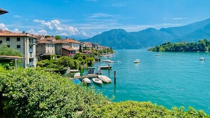 A lakeside village with buildings along the shore, boats docked at the pier, and mountains in the background.