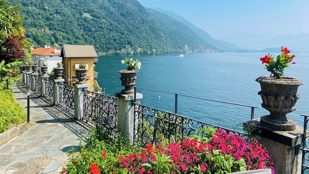 A scenic lakeside pathway with stone steps, metal railings, and potted plants.
