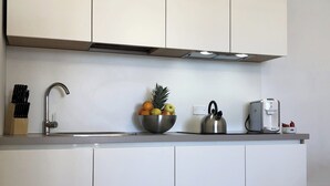 A modern kitchen with white cabinets, a stainless steel sink, a kettle, a coffee maker, and a bowl of fruit on the counter. - Apartment 2+2 with panoramic terrace (201) (LAVARONE)
