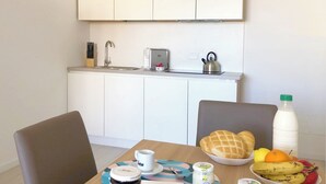 A modern kitchen with white cabinets, a sink, and a toaster. There is a dining table with a bowl of fruit, a bottle of milk, and a jar of jam. - Apartment 2+2 with panoramic terrace (201) (LAVARONE)