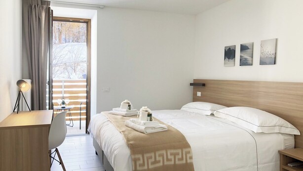 Una habitación de hotel con cama, escritorio, silla y ventana con cortinas.
