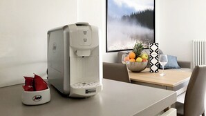Una habitación de hotel moderna con una cafetera, un bol de fruta y un cuadro en la pared.