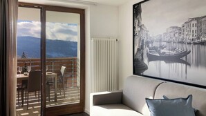 Une pièce avec un balcon, un canapé, une table avec des chaises et un tableau représentant un paysage de canal.