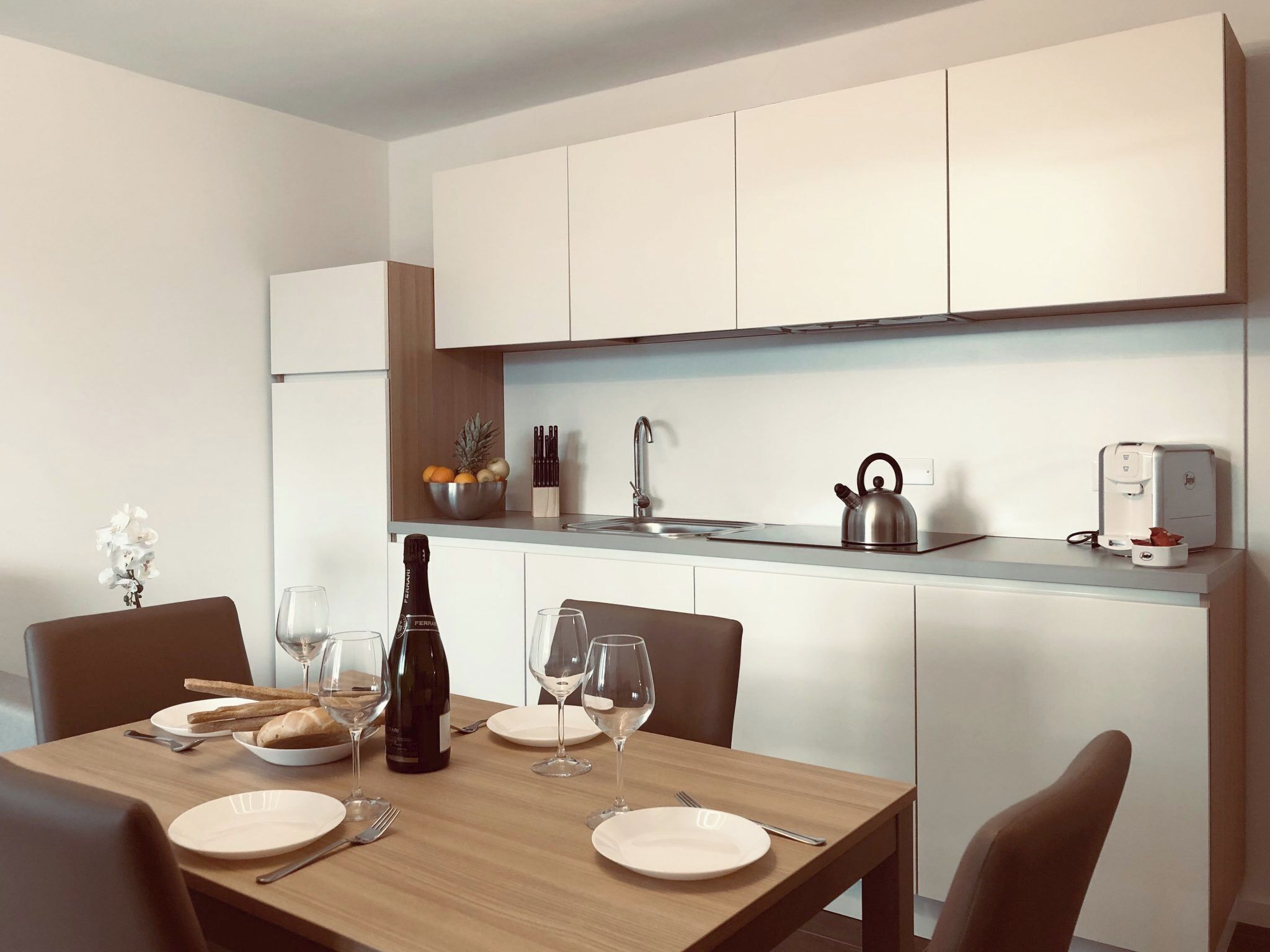 A modern kitchen with white cabinets, a stainless steel kettle, and a coffee machine.