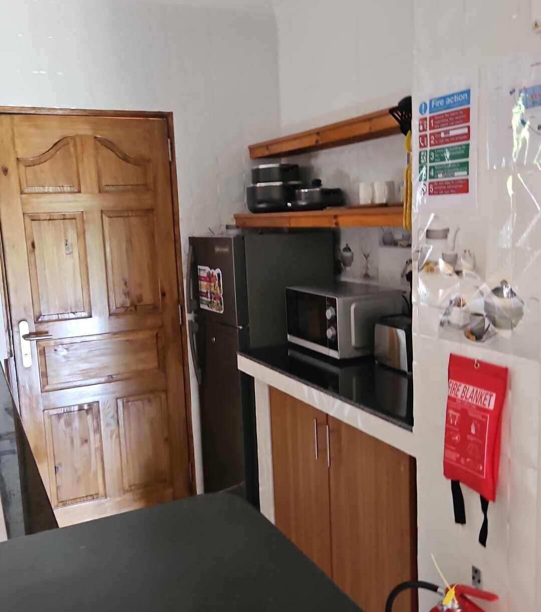 Een keuken met houten kastjes, een magnetron, een broodrooster en een branddeken aan de muur.