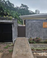 Una entrada cerrada con rampa que conduce a un edificio, rodeado de vegetación y un cartel que indica servicios de cocina propia.