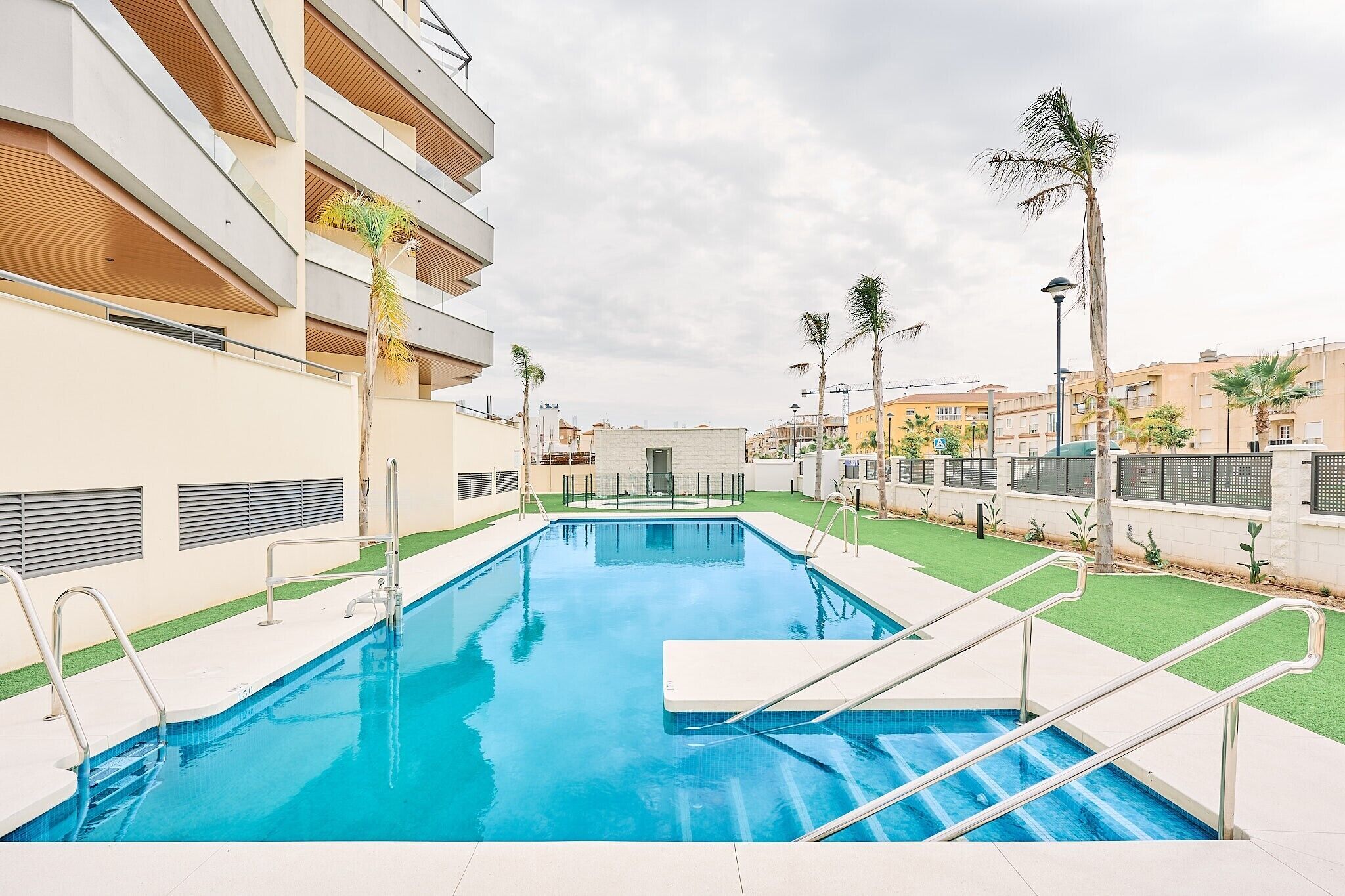Une piscine à l’eau d’un bleu cristallin, entourée d’un bâtiment moderne doté de balcons et de palmiers.
