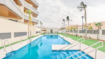 Une piscine à l’eau d’un bleu cristallin, entourée d’un bâtiment moderne doté de balcons et de palmiers.