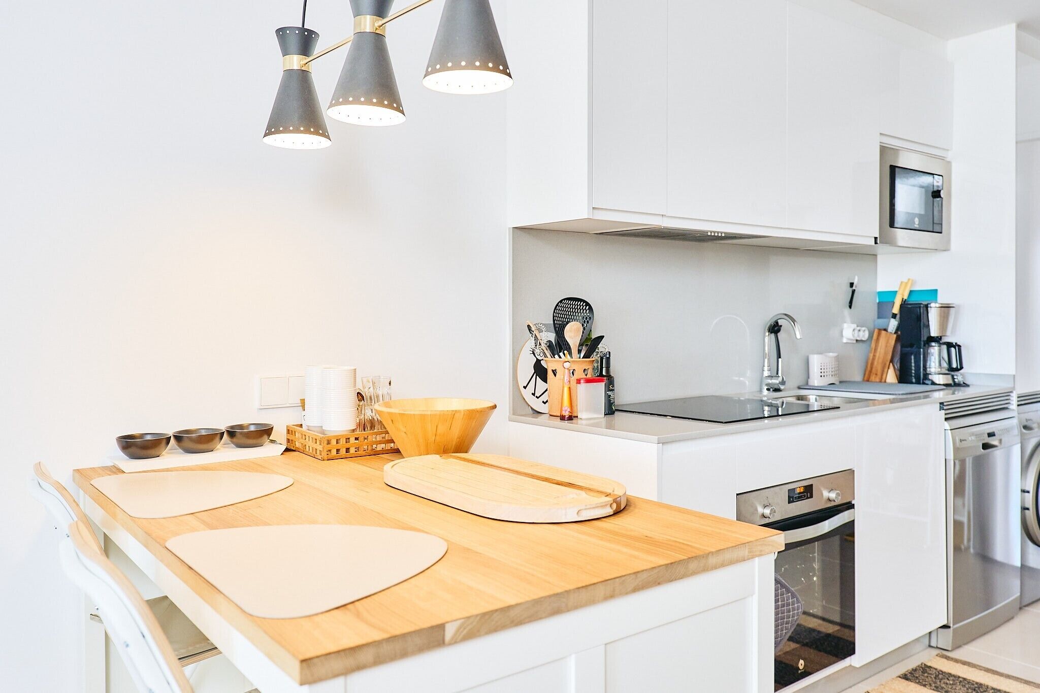 A modern kitchen with white cabinets, a wooden countertop, a microwave, a sink, and a stove.