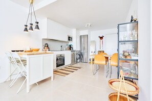Una cucina moderna con mobili bianchi, un'isola centrale e un'area pranzo con sedie gialle.