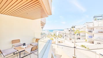 A balcony with a wooden ceiling, a table with chairs, and a view of a coastal residential area.