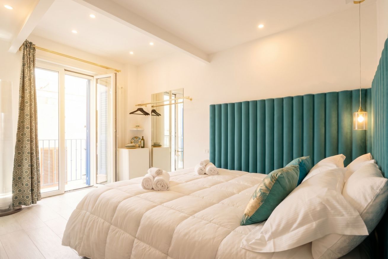 A bedroom with a large bed, a mirror, a wardrobe, and a balcony.