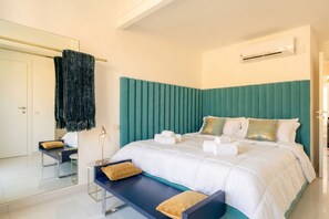 Ein modernes Schlafzimmer mit einem türkisfarbenen Kopfteil, einem Bett mit weißer Bettwäsche, einer Bank mit Kissen und einem Spiegel an der Wand.
