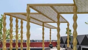 Eine Dachterrasse mit einem pergolaartigen Überdachung aus geometrischen Mustern, Sitzgelegenheiten im Freien und Blick auf die Skyline.