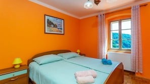 Un dormitorio con cama, un cuadro, una ventana con cortinas y una lámpara.