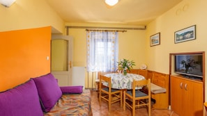 Una habitación pequeña y acogedora con sofá, una mesa de comedor con sillas, televisor y ventana con cortinas.