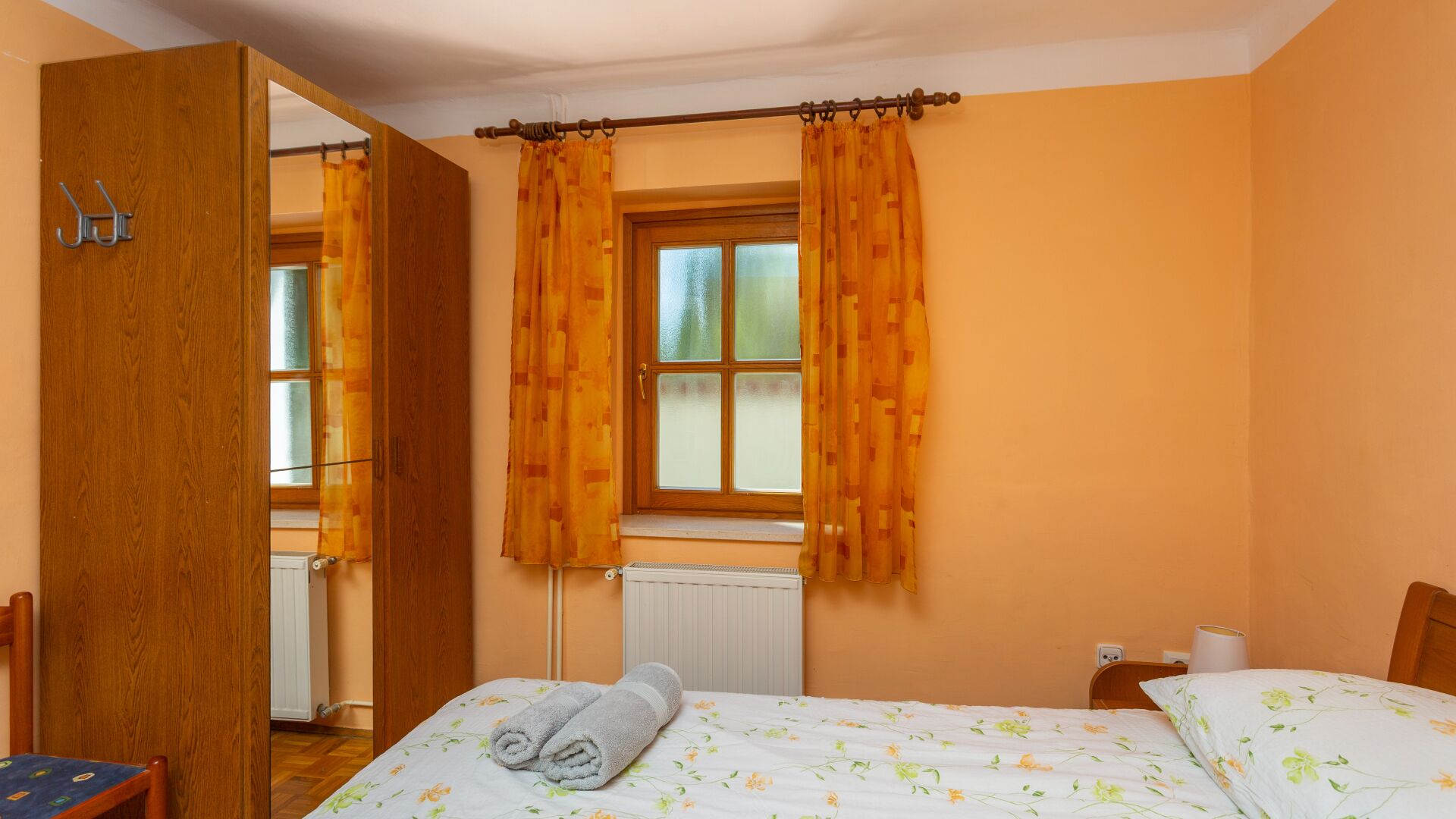 Une chambre à coucher avec un lit, un radiateur, une fenêtre avec des rideaux et une porte en bois.