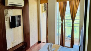 A hotel room with a bed, a television mounted on the wall, an air conditioning unit, and a view of the outdoors through the window. - Hotel Raj Villa (Jodhpur)