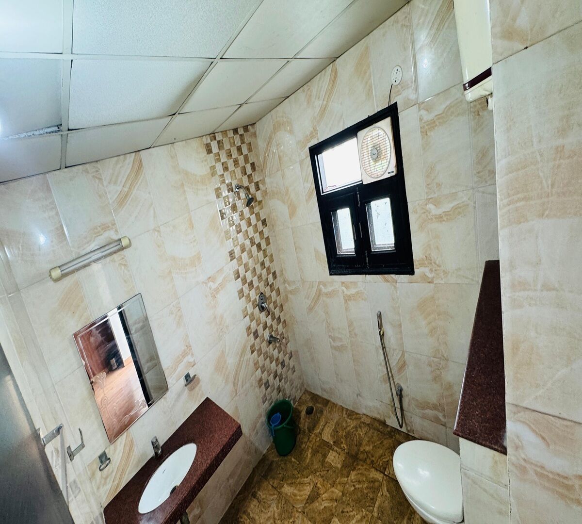 A bathroom with a marble floor, a sink, a toilet, a mirror, and a shower area.