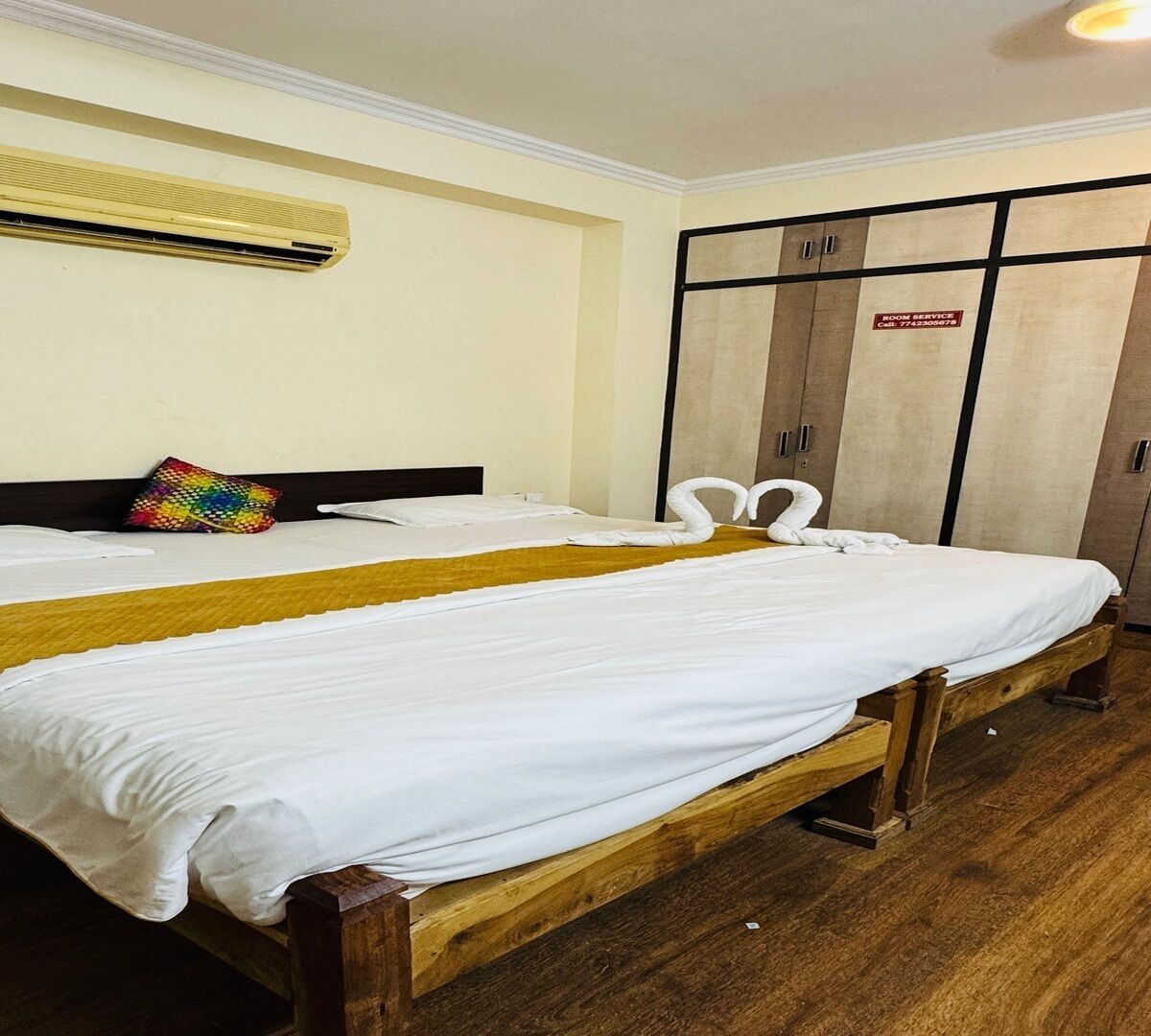 Una camera d'albergo con due letti singoli, pavimento in legno, climatizzatore a parete e un armadio con il cartello 'Room Service'.