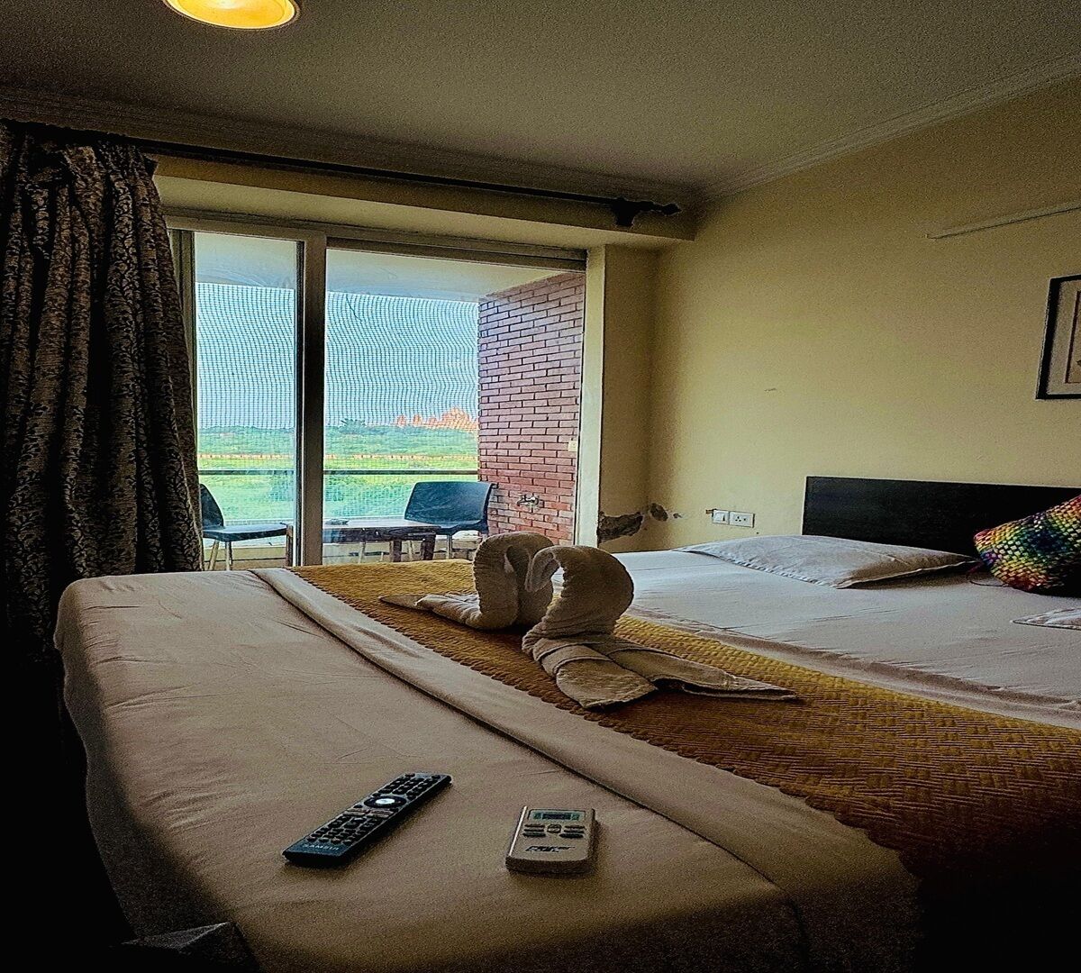 A hotel room with a bed, a bench, a remote control, and a mobile phone on the bench.