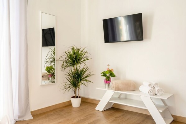 A modern bathroom with a wooden floor, a white vanity, a potted plant, a mirror, and a flat-screen TV.