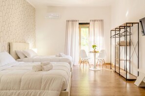 Habitación de hotel con dos camas, una mesita con sillas, perchero y ventana con cortinas.