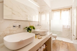 Un baño moderno con dos lavamanos tipo pedestal, un espejo y una zona de ducha.