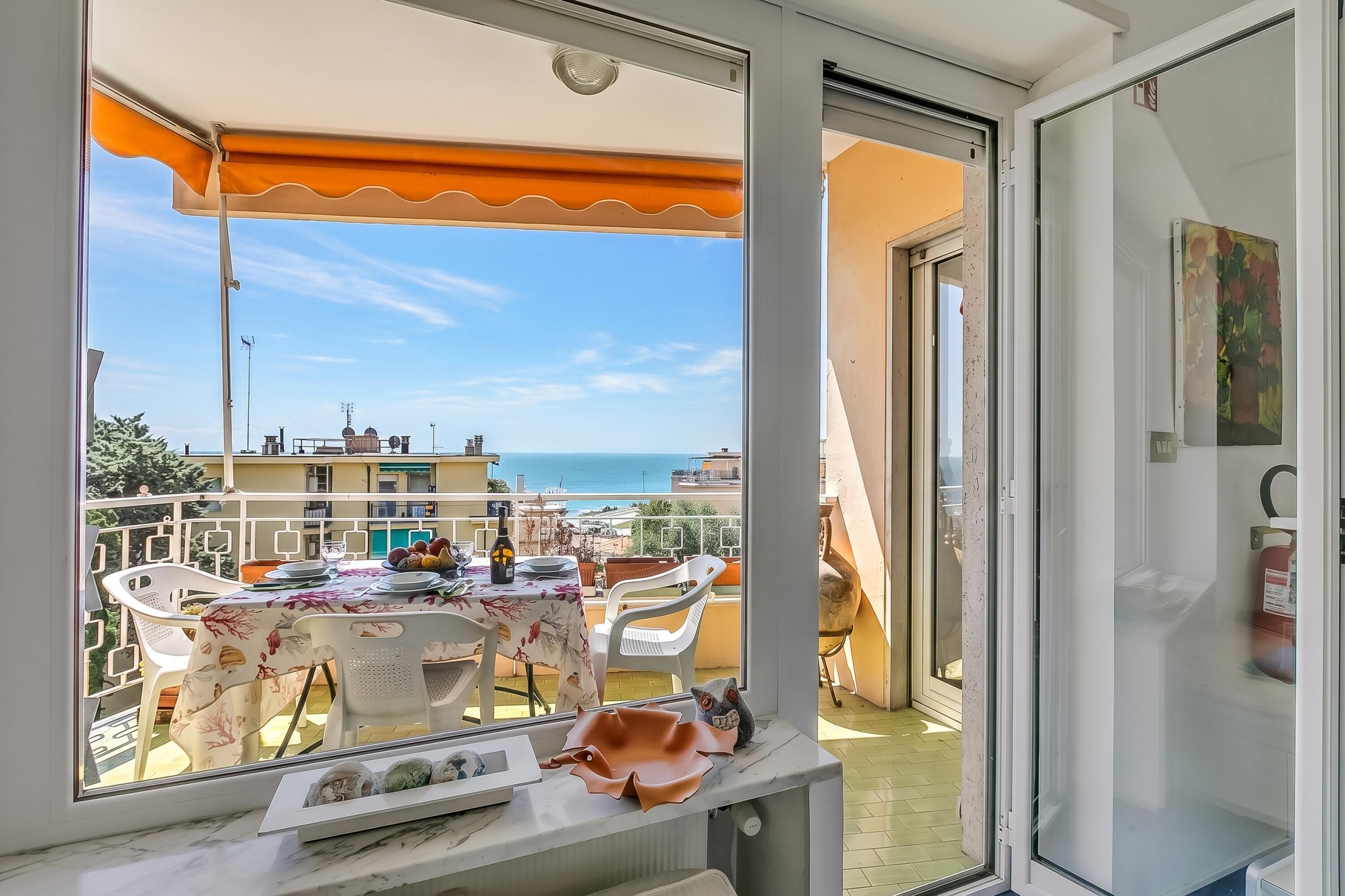 Un balcón con una mesa dispuesta para comer, vista al mar y una puerta que da al interior.