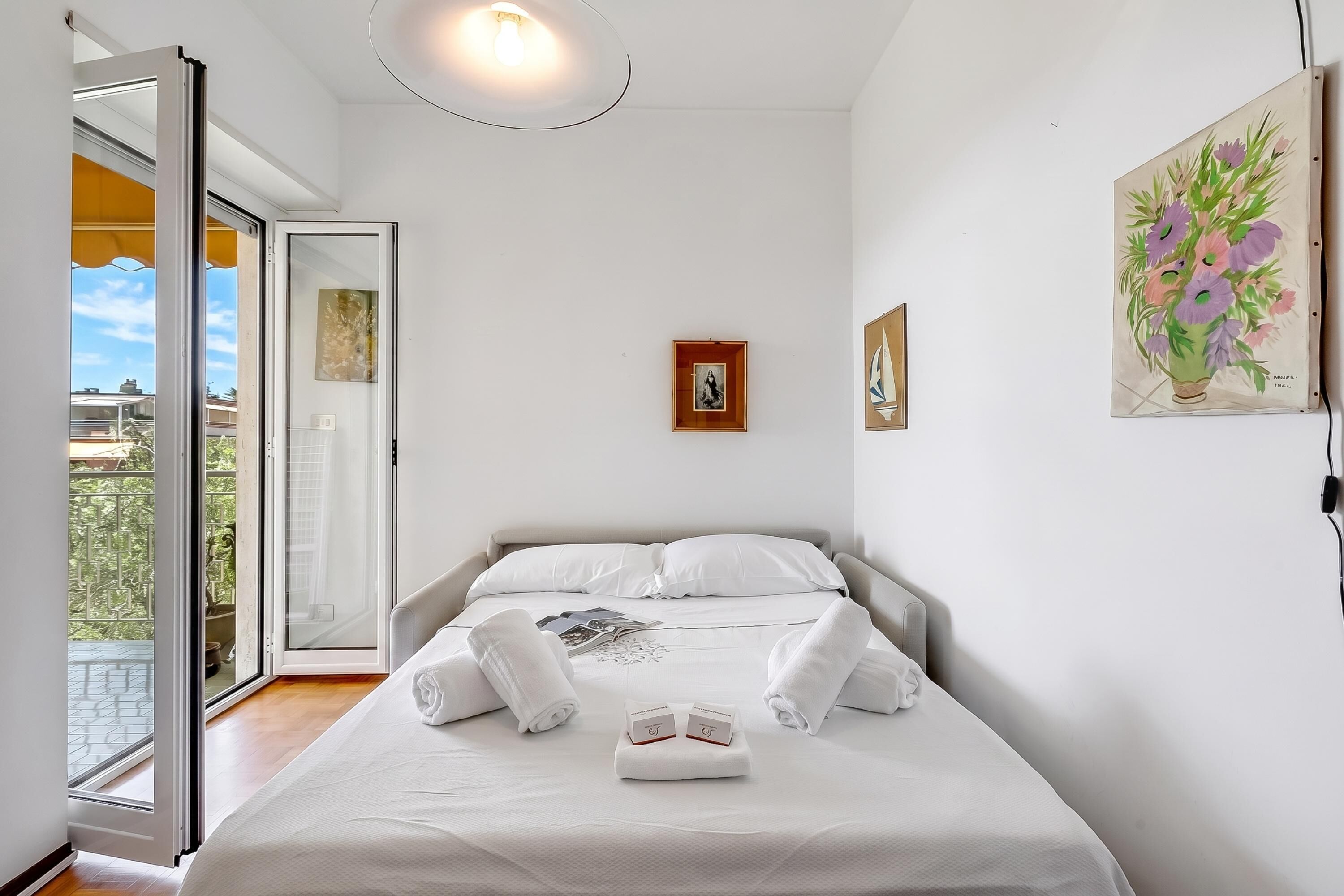 A bedroom with a bed, a painting, and a window with a view.