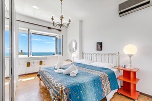 A hotel room with a bed, a bedside table with a lamp, a window with a view, a ceiling fan, and a wall-mounted air conditioning unit. - Owl House, Sea-view Terrace Apt in Sanremo (Sanremo)