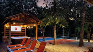Una cancha de tenis al aire libre con un pabellón de madera, sillas de descanso y un jacuzzi.