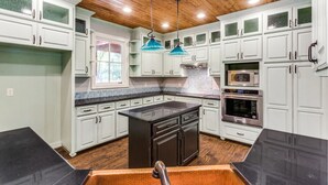 Una cocina moderna con armarios blancos, una isla central, electrodomésticos de acero inoxidable y techo de madera.