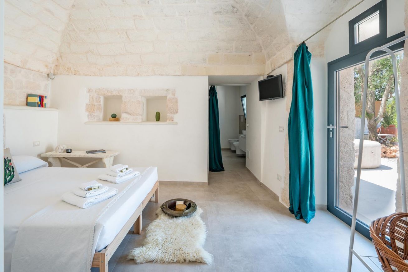 Ein Schlafzimmer mit einem Bett, einem kleinen Tisch, einem Fernseher und einem durch eine offene Tür einsehbaren Badezimmer.