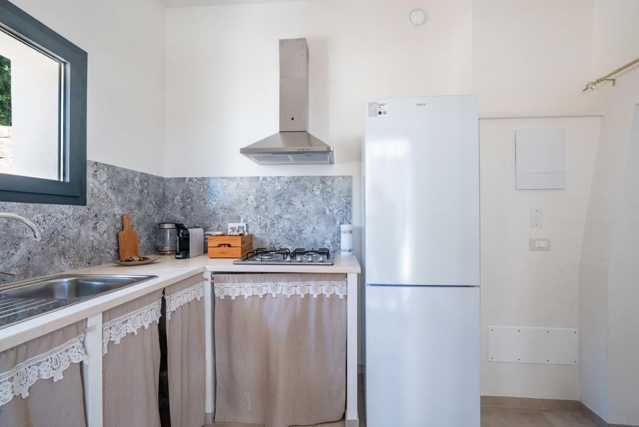 A kitchen with a stainless steel range hood, a white refrigerator, a window with a view, and a sink.