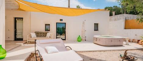 Un espacio exterior moderno con una silla lounge blanca, un jacuzzi y una vela amarilla.