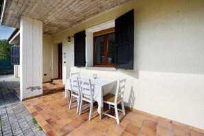 A patio with a table and chairs, a window with shutters, and a tiled floor.