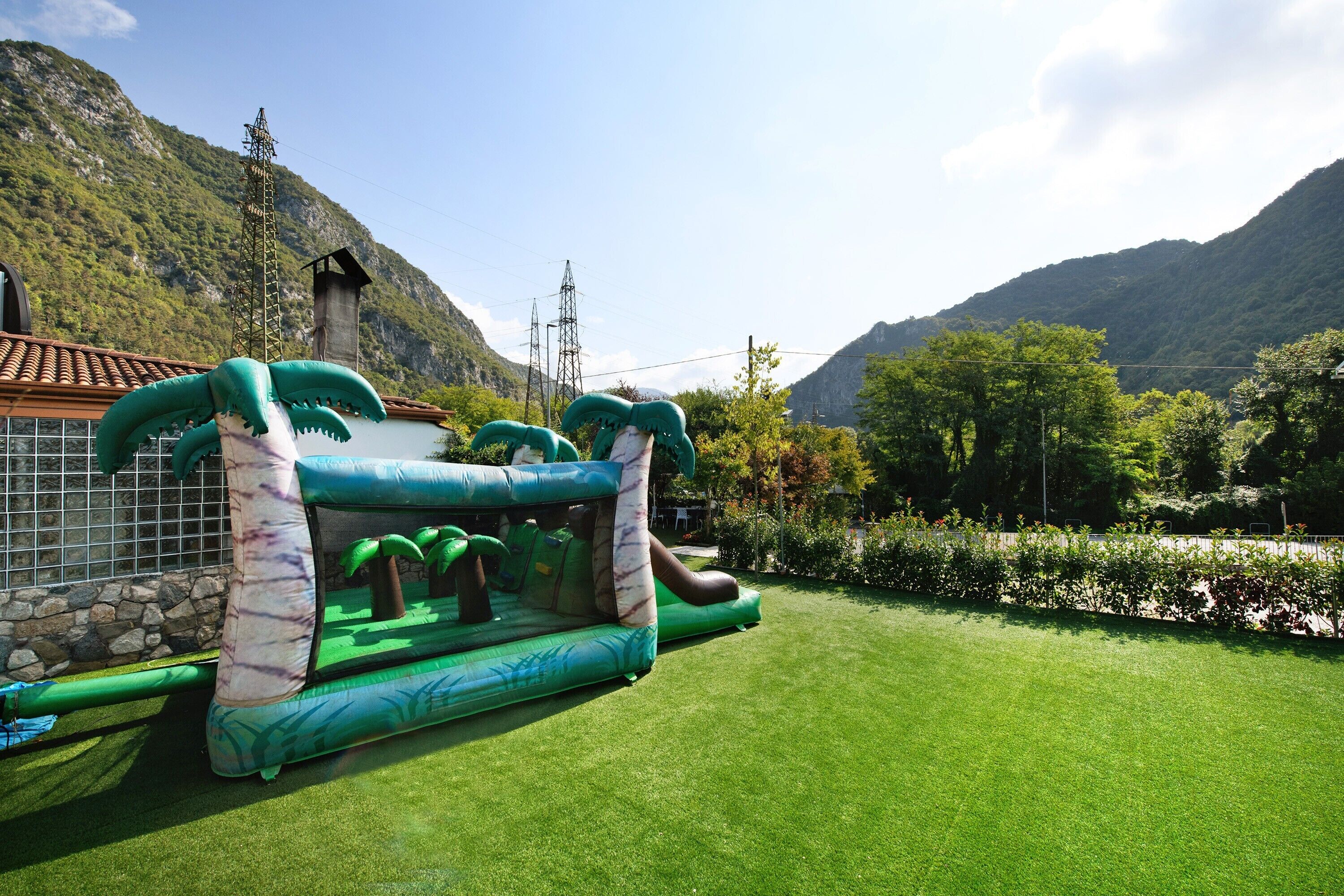 Un área de juegos inflable con toboganes y pared de escalar, frente a un paisaje de montañas y cielo despejado.